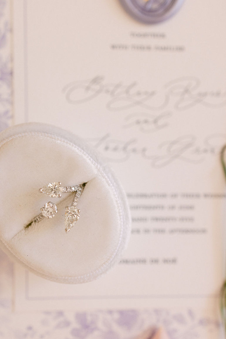 Photographie poétique de Margaux Kanarek : la bague de fiançailles Laetitia, création sur mesure en or blanc 18 carats, repose dans son écrin sur un faire-part de mariage – symbole d’amour et de transmission signé DM Jeantet Joaillerie.