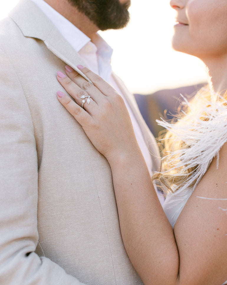 Création à la demande : bague de fiançailles en or blanc 18 carats, sertie de deux diamants poires et d’un diamant rond – pavage brillant signé DM Jeantet Joaillerie. Photographie de couple par Margaux Kanarek.